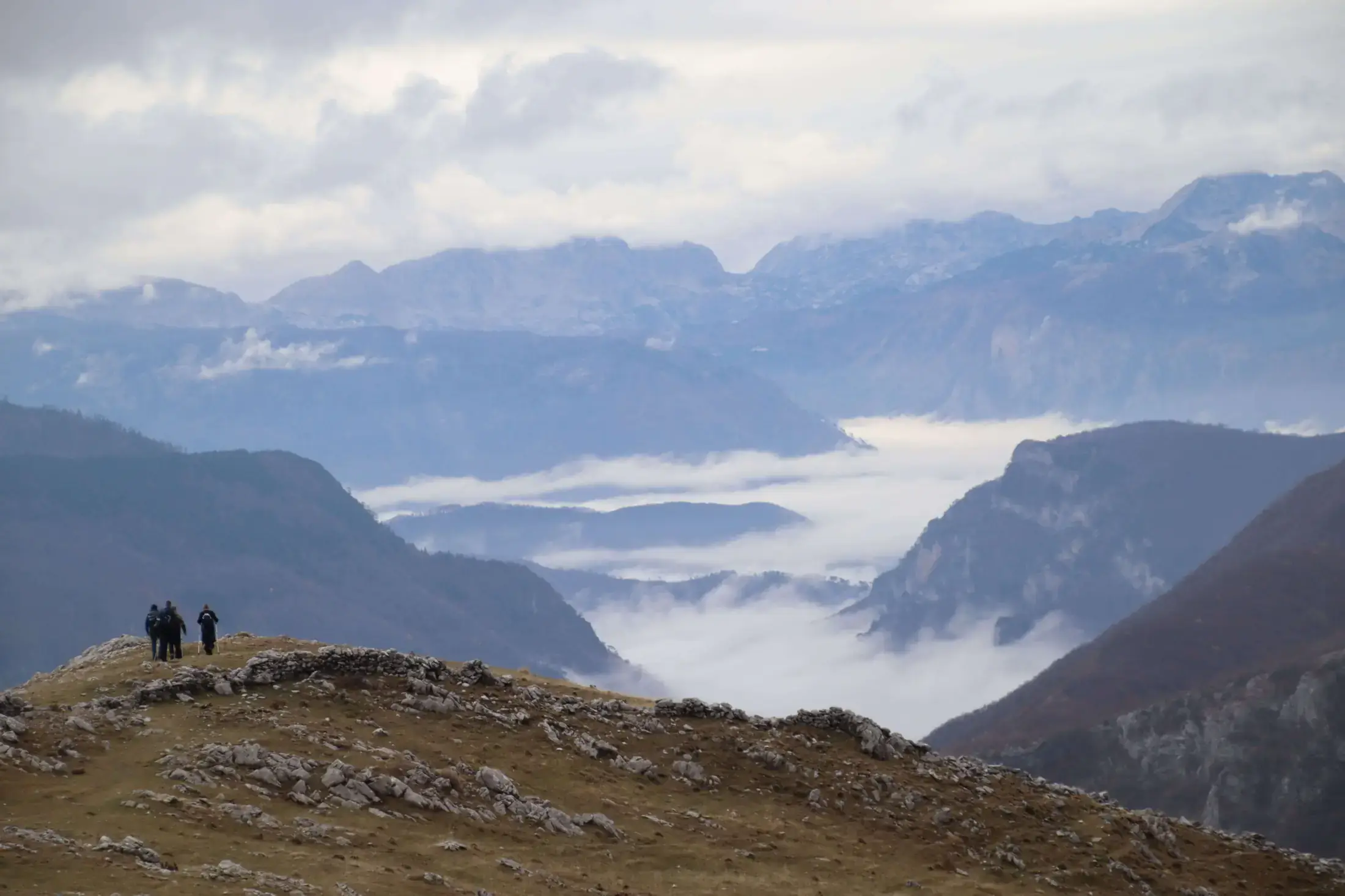 Hikers on a ridge above cloud-filled valleys near Lukomir