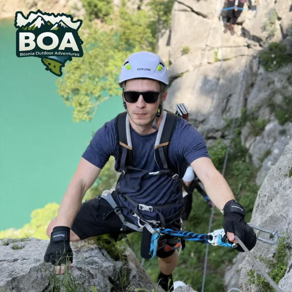 Rahmo climbing above a turquoise lake on a via ferrata route
