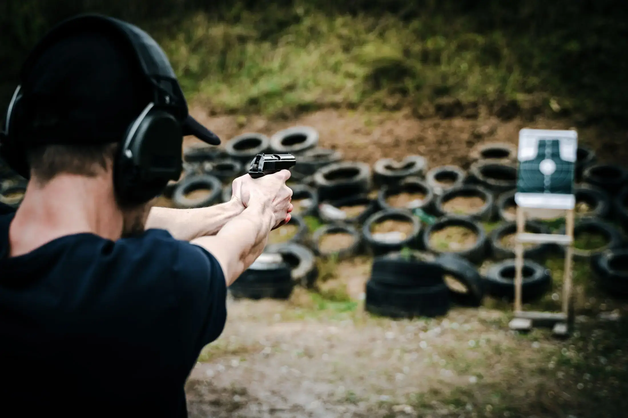 A shooter with ear protection aiming at a target on an outdoor range